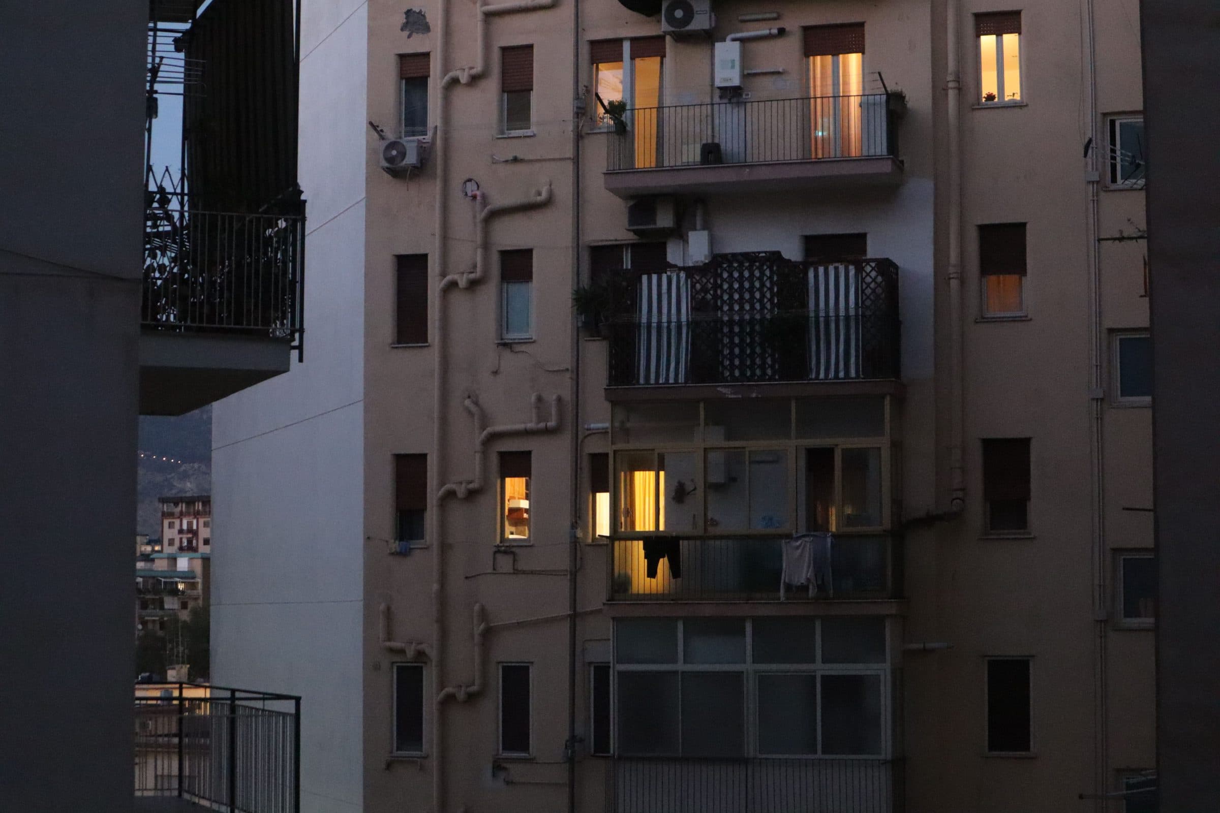 Apartment balconies stacked up a dark facade with a few lights on