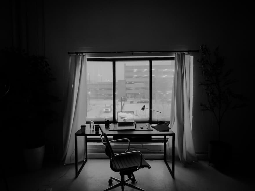 An empty desk and chair in front of a bright office window