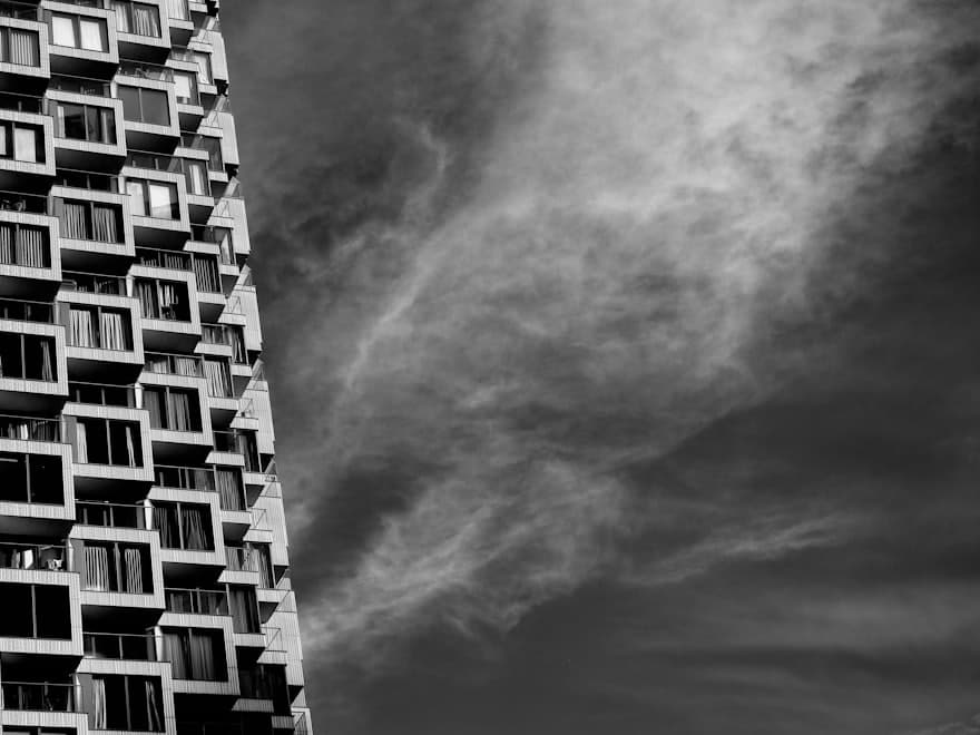Black-and-white apartment facade, dozens of windows against a dramatic sky
