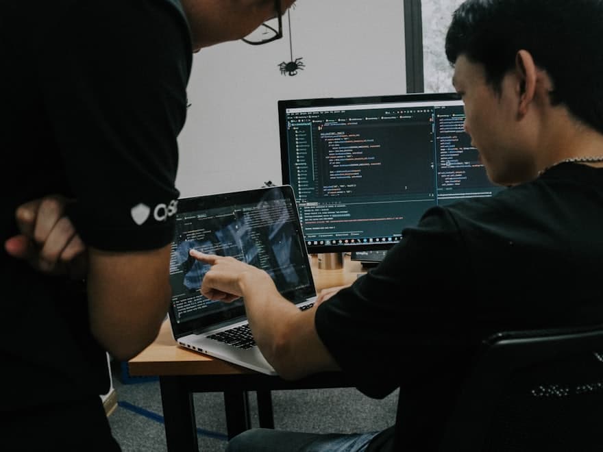 Two developers at one screen, one pointing at the code
