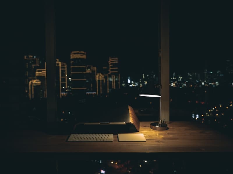 A desk lamp lighting a laptop, with a city skyline at night behind it