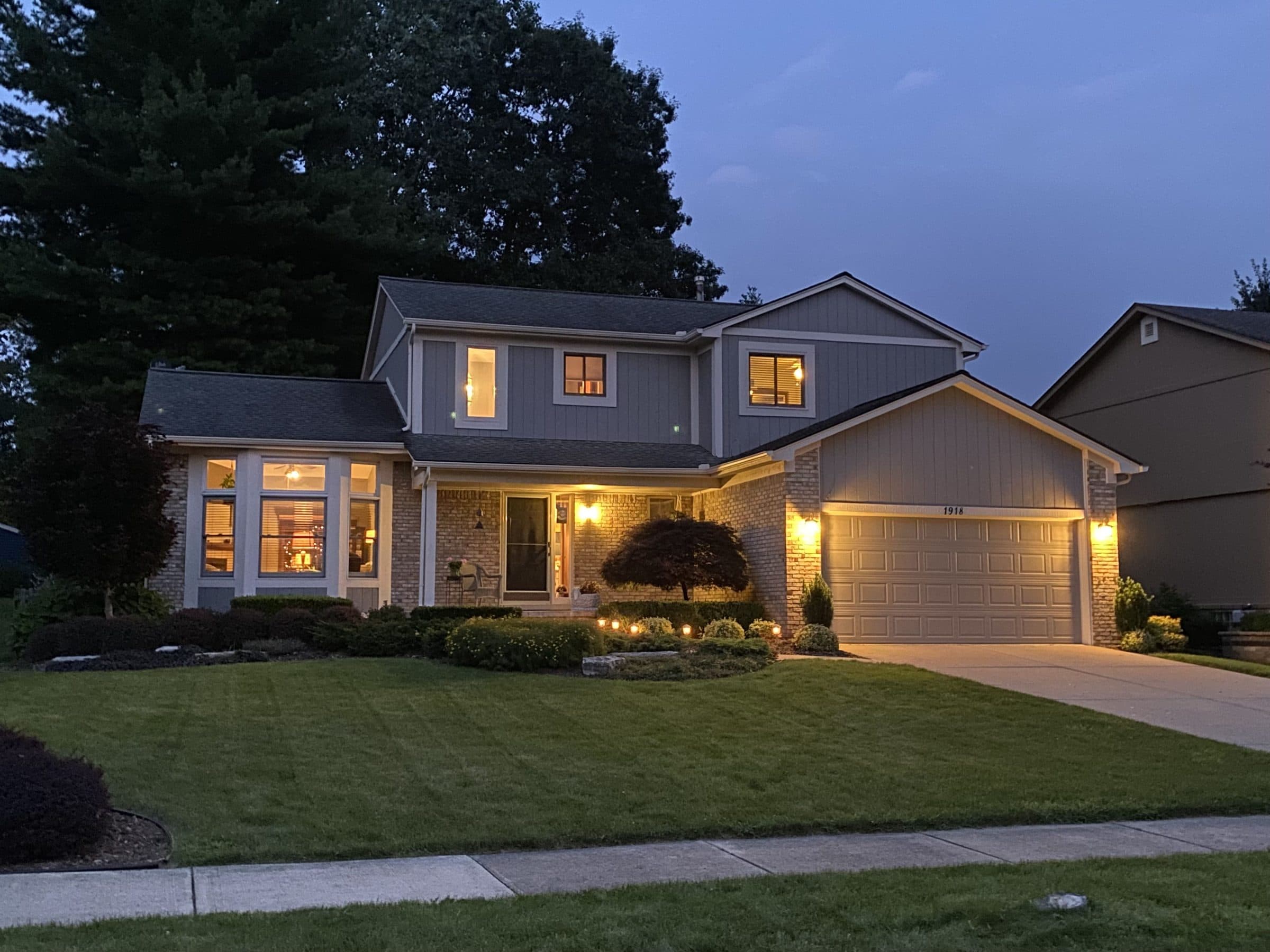 Row of single-family houses on a quiet American street at dusk, porch lights on