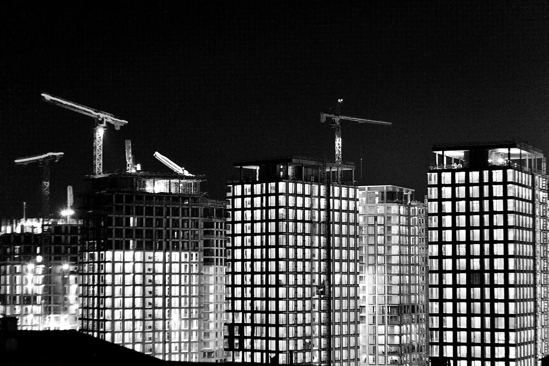 Tower cranes over a cluster of lit apartment blocks under construction at night