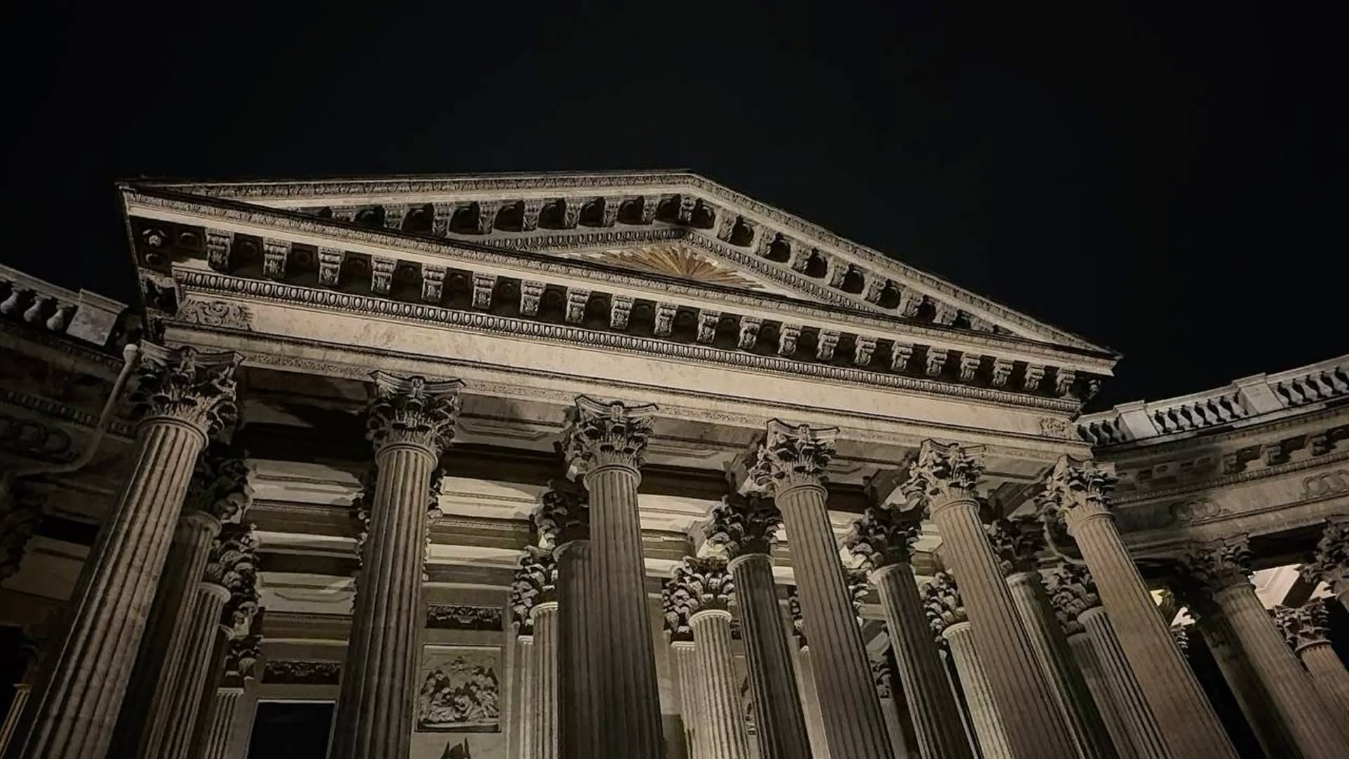 Stone columns of a classical exchange building lit from below at night