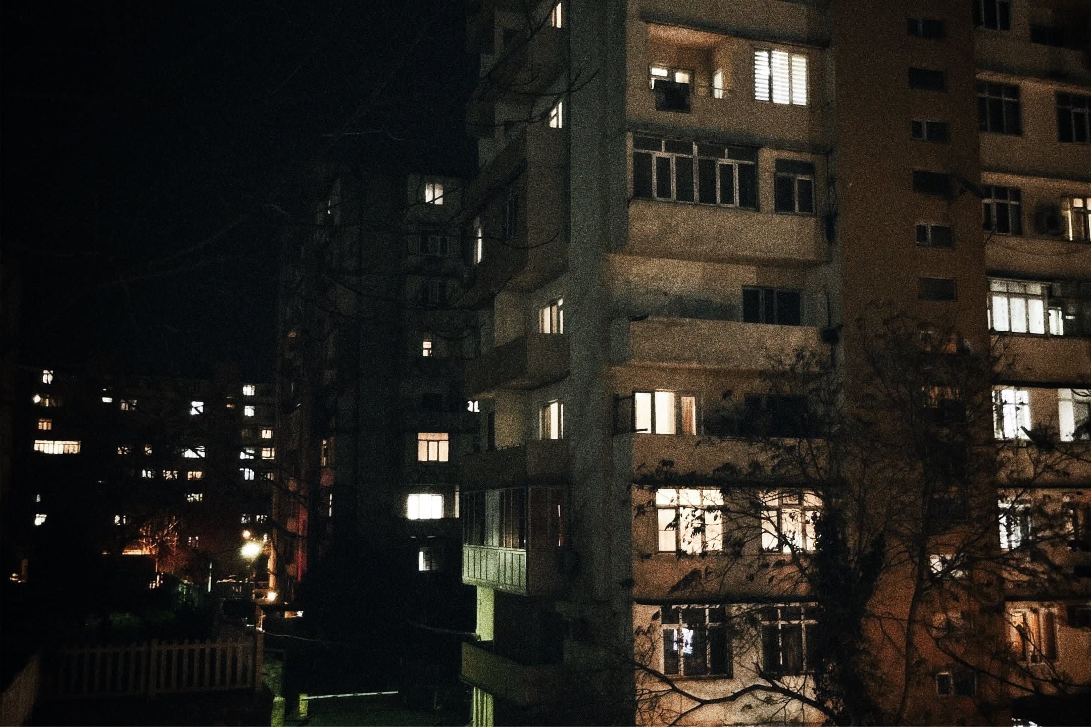 Apartment block at night with a few windows lit among many dark ones