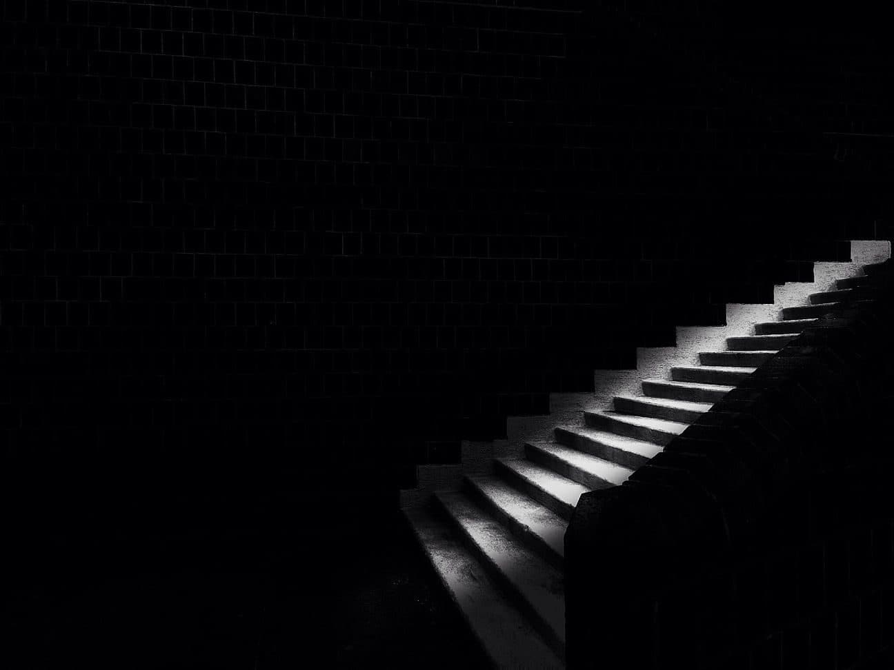 A single lit staircase rising through a dark room
