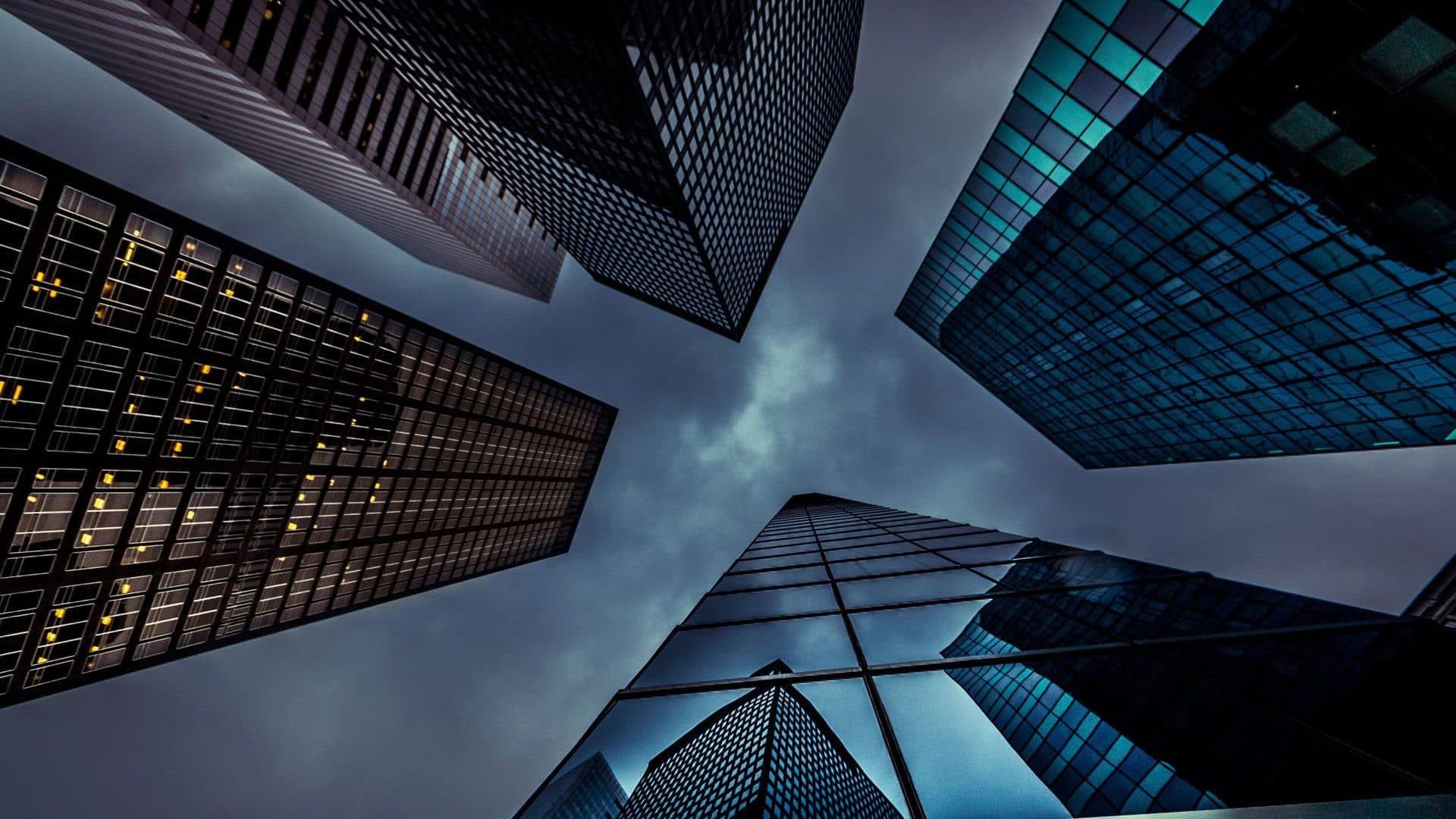 Looking up between mirrored glass towers under a stormy sky