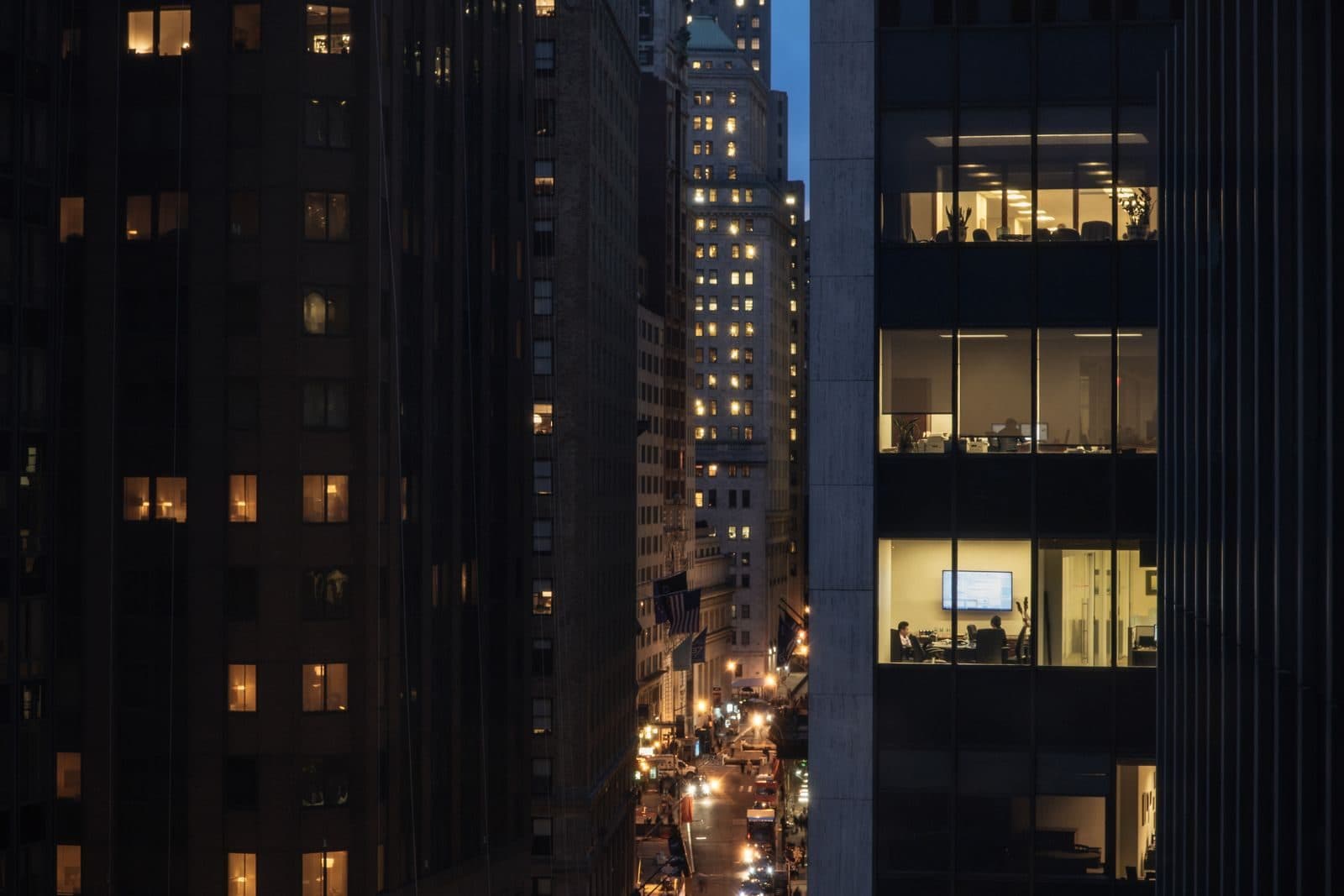 Corner of an office tower at night with a handful of windows lit