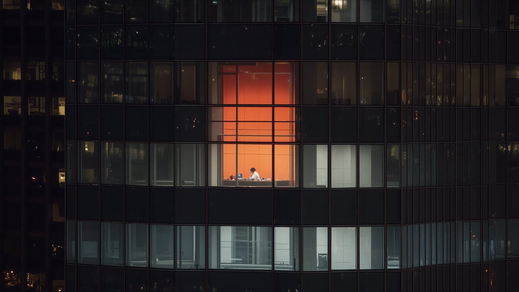 Dark office facade with a single window lit in orange