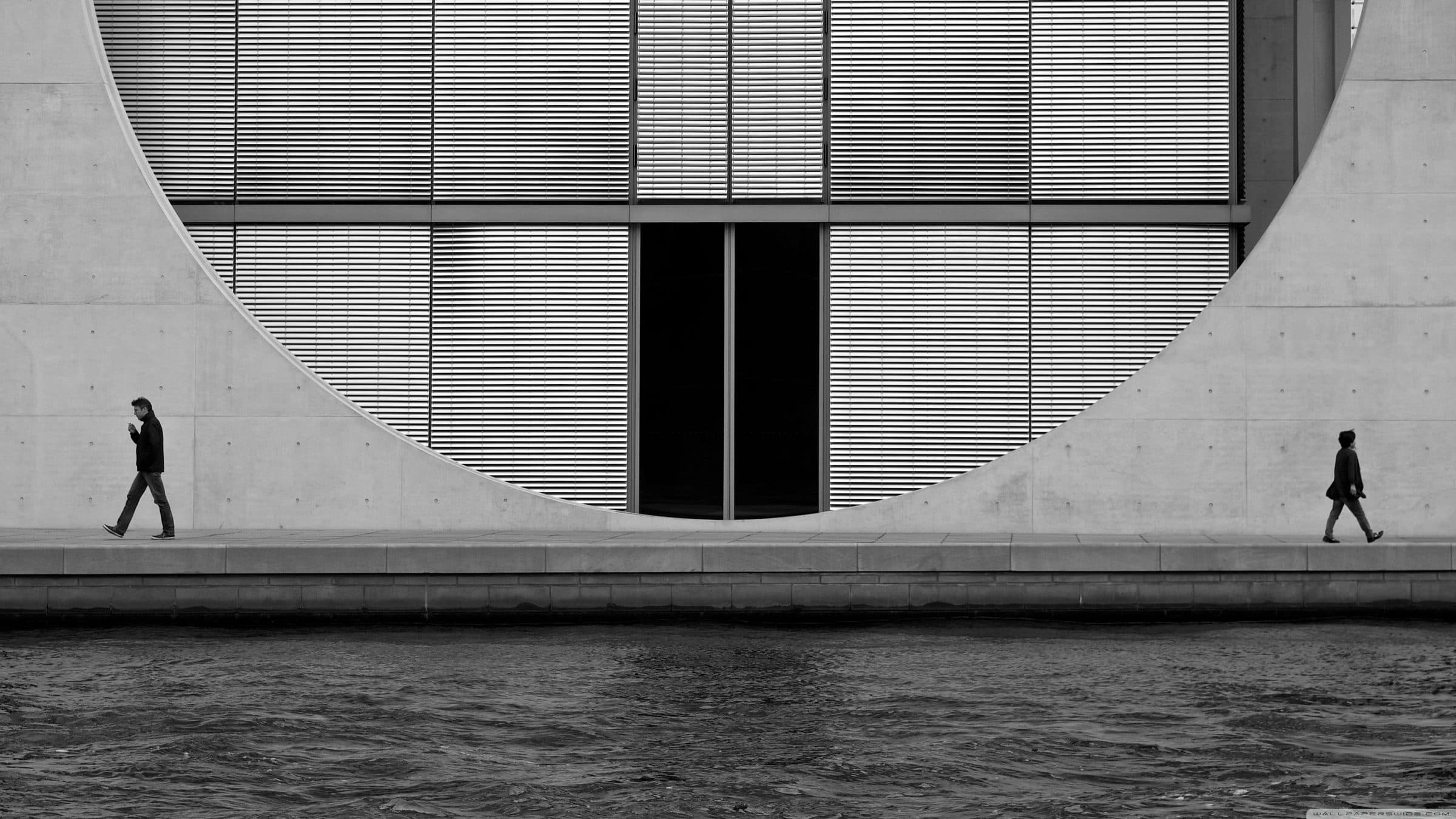 Two figures walking beneath a huge circular concrete facade
